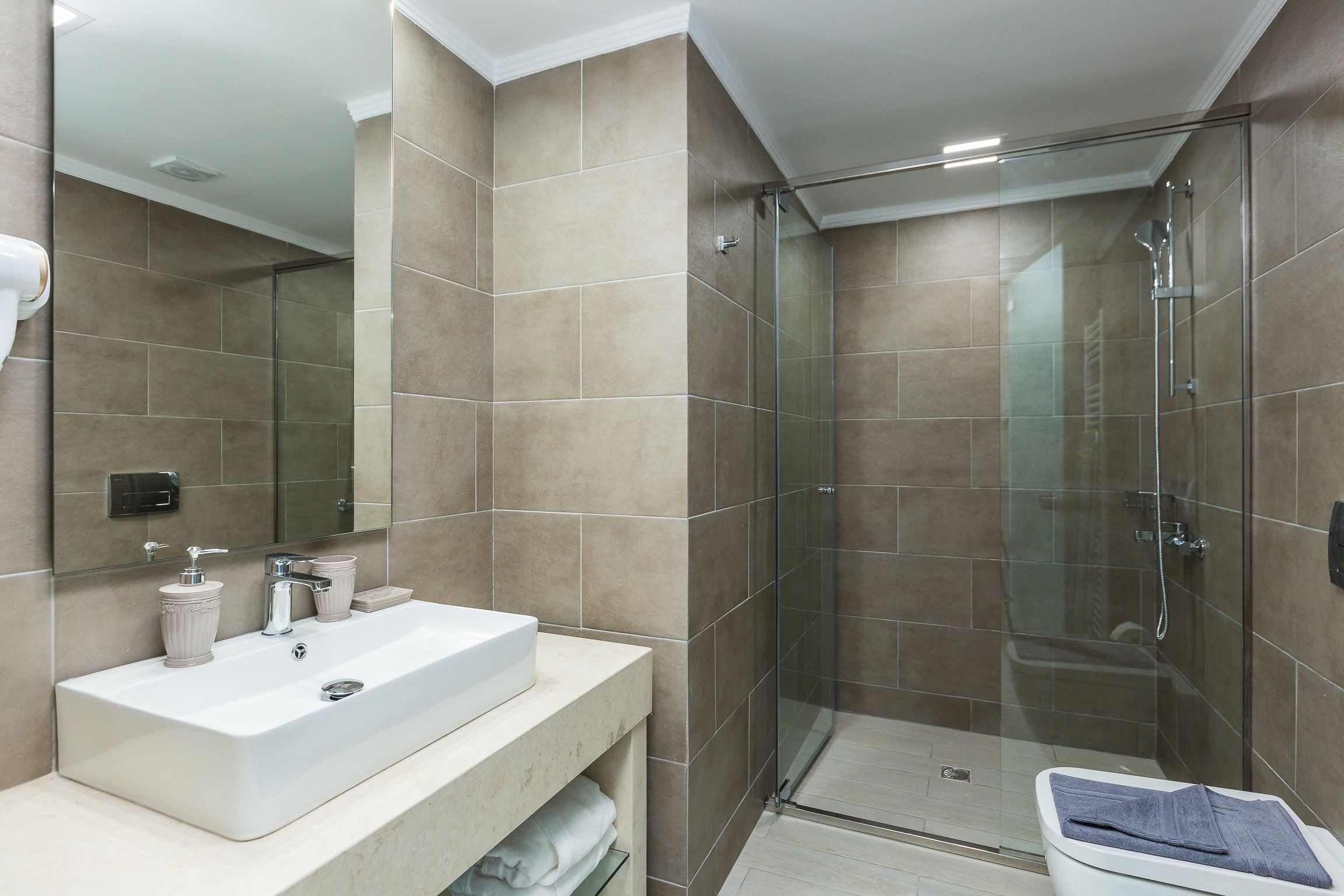 Een moderne badkamer met een douchecabine van glas, een groot wastafelmeubel en een spiegel.