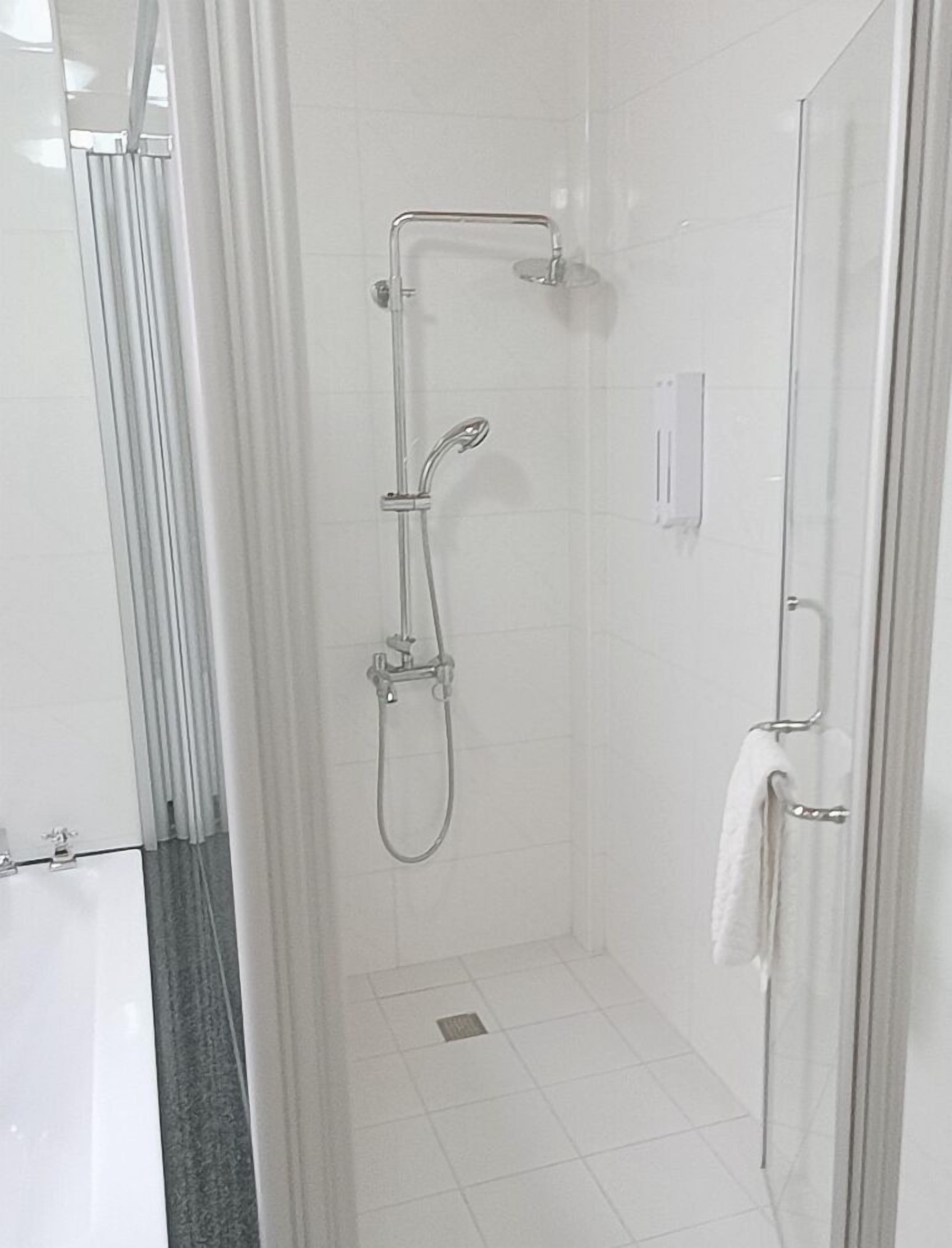Un área de ducha pequeña y cerrada con puerta de vidrio, un cabezal de ducha manual y un perchero para toallas.