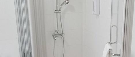 Un área de ducha pequeña y cerrada con puerta de vidrio, un cabezal de ducha manual y un perchero para toallas.