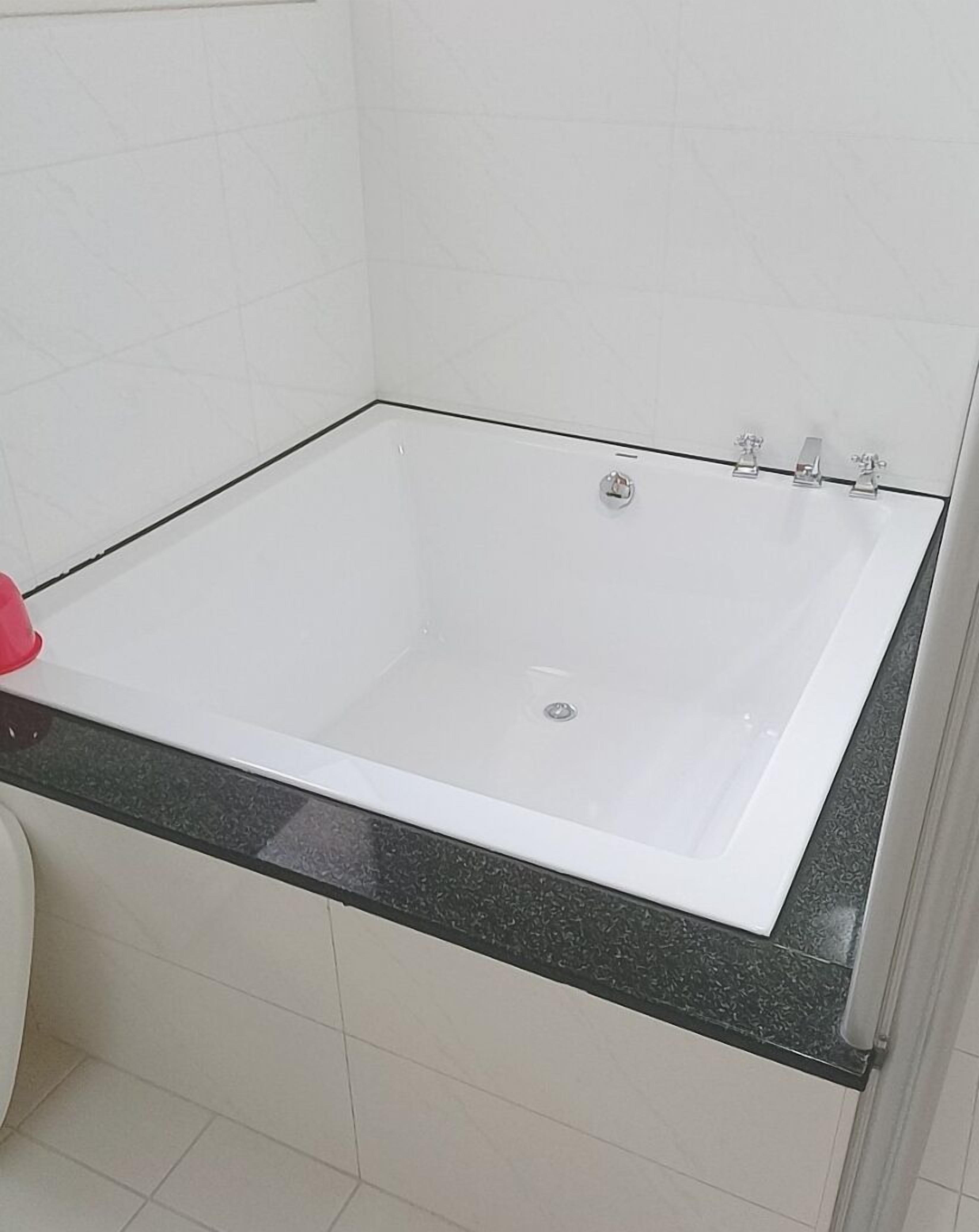 Un baño con una bañera blanca, encimera negra y paredes de azulejos blancos.