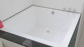 A bathroom with a white bathtub, a black countertop, and white tiled walls.