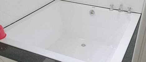 Un baño con una bañera blanca, encimera negra y paredes de azulejos blancos.