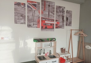 A room with a wall-mounted shelf holding kitchen utensils, a small sink, and a red storage box.