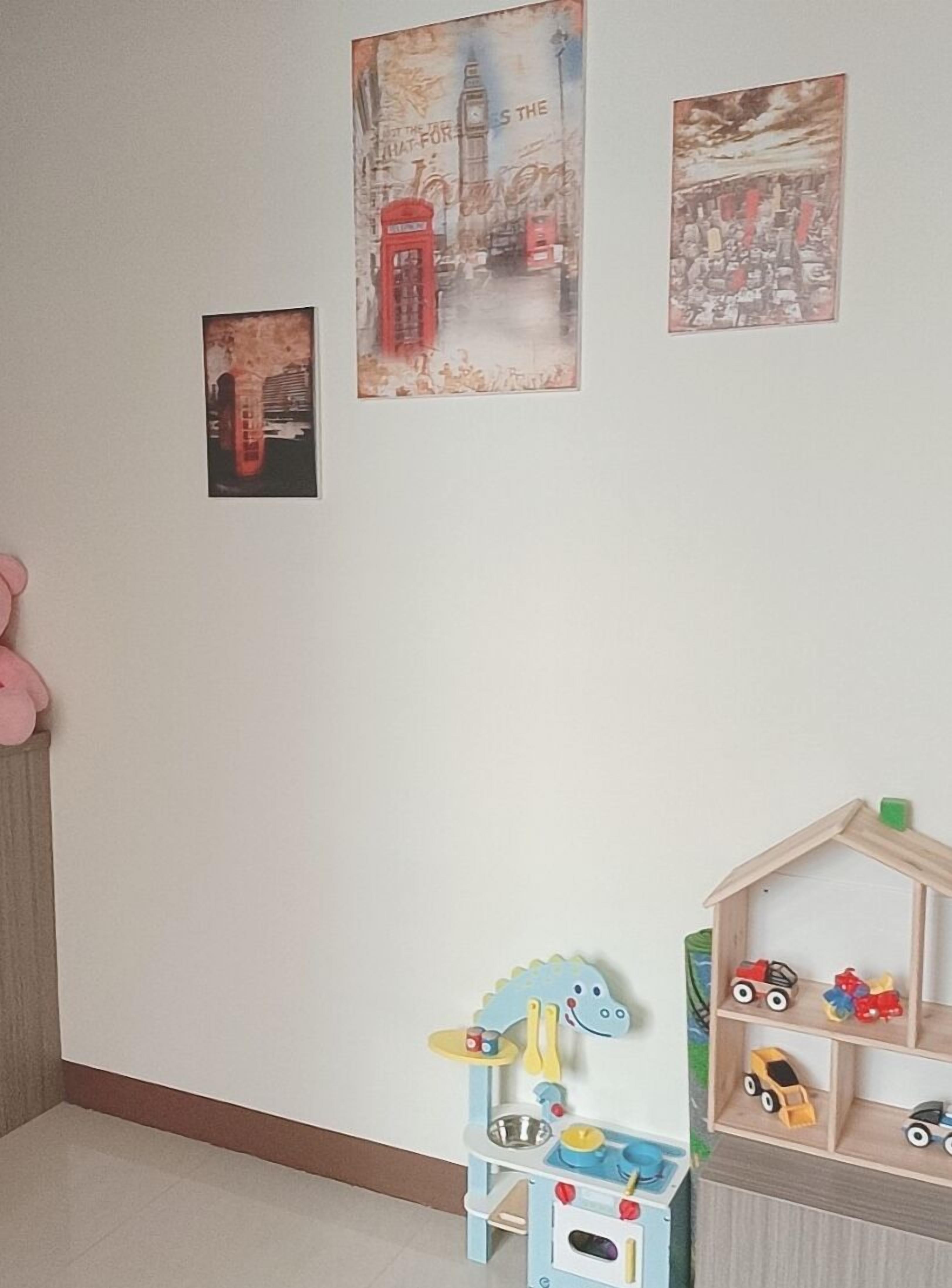 Uma área de recreação infantil com um cavalinho de brinquedo, uma casinha e uma parede com três quadros.