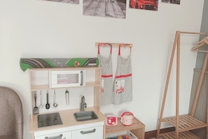 A compact kitchenette with a microwave, sink, and small stove. There are hanging utensils and a wooden rack.