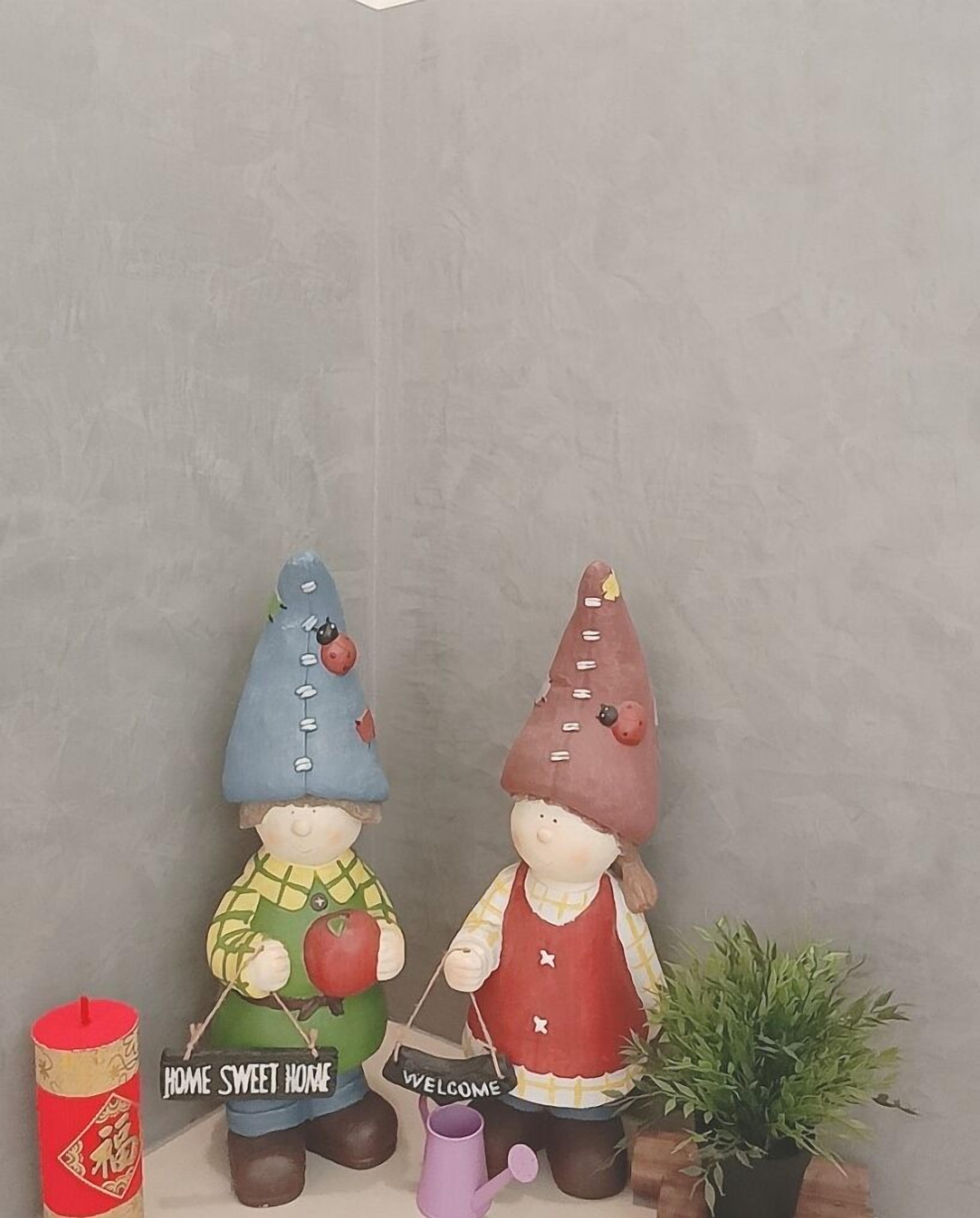 Deux figurines décoratives représentant des gnomes, chacune tenant une pancarte, une bougie rouge et une plante en pot.