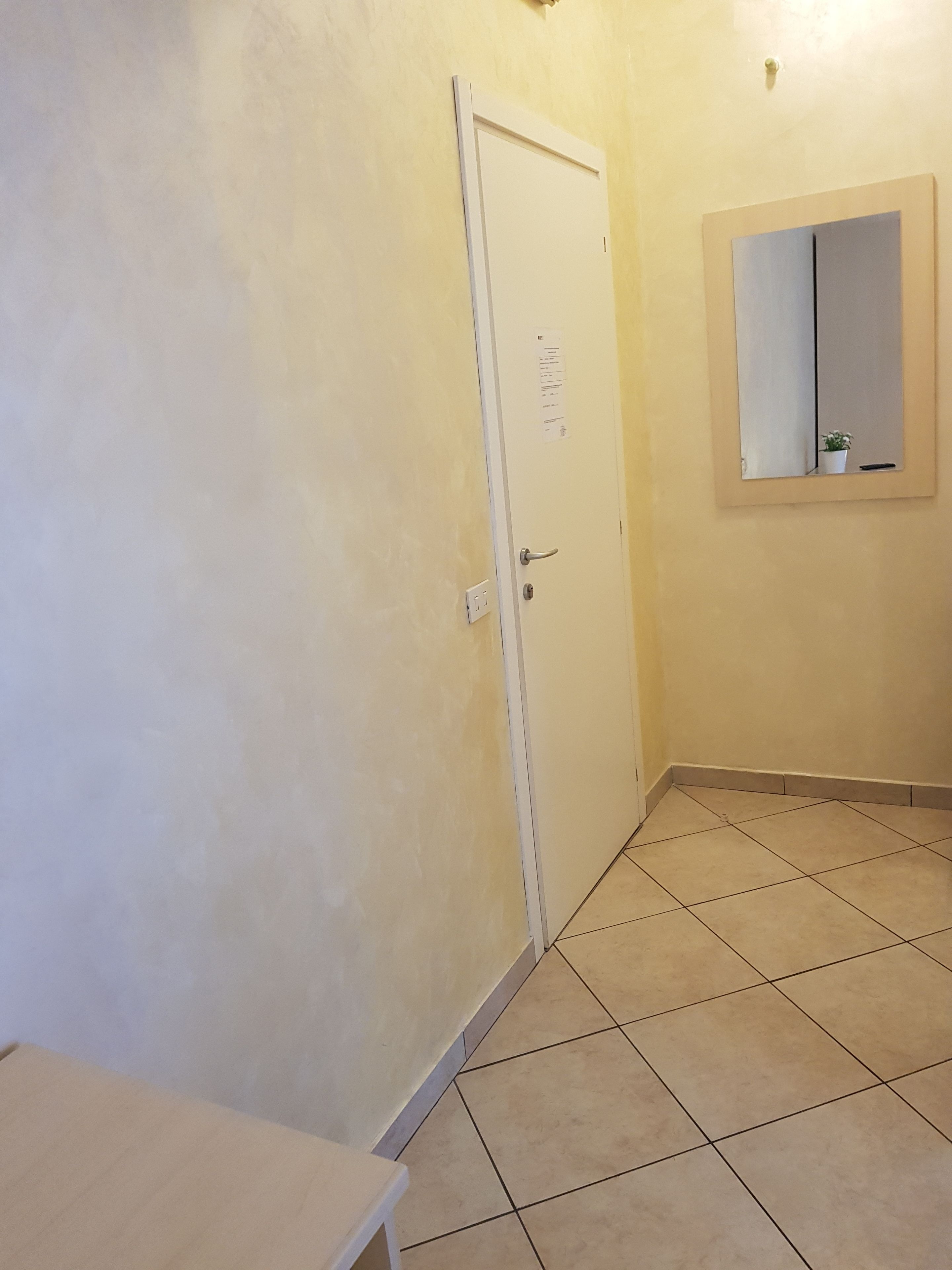 A small, clean room with a white door, a small table, and a mirror on the wall.