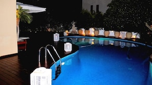 An outdoor swimming pool with a wooden deck, surrounded by potted plants and a white umbrella. - Paradise Villa Sounio (Saronikos)