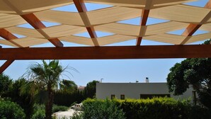 A covered outdoor area with a wooden structure and a view of a modern building in the background. - Paradise Villa Sounio (Saronikos)