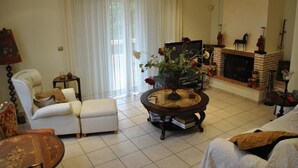 A living room with a fireplace, a sofa, a chair, and a coffee table. - Paradise Villa Sounio (Saronikos)