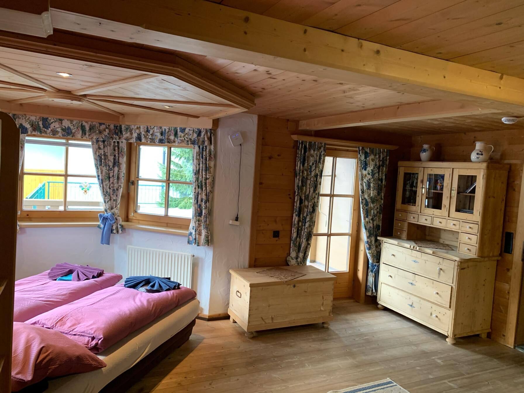 Una habitación de madera con cama, cómoda y ventana con cortinas.