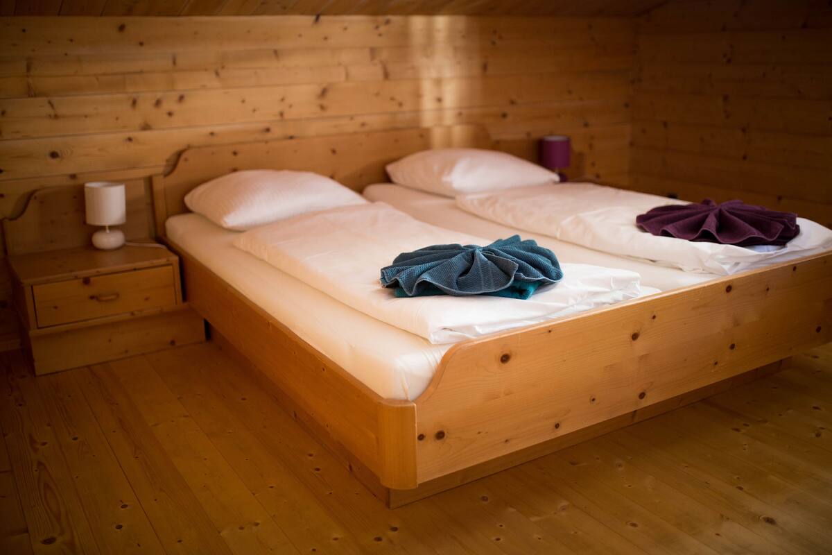 Quarto de cabana de madeira com cama, mesa de cabeceira e abajur.