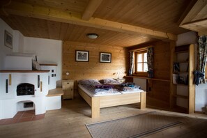A wooden cabin bedroom with a bed, a fireplace, and a window with curtains. - Landhaus Erlzette (Tux)