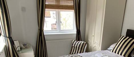 A bedroom with a bed, a wardrobe, a radiator, a window with curtains, a bedside table, and a hanging light fixture.