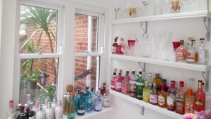 A room with a window overlooking a brick wall and a plant. There are shelves with various bottles and glasses. - Jireh House (Yarmouth)