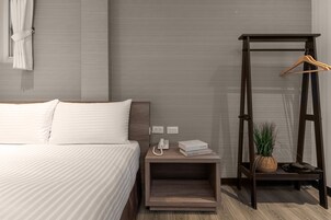 Un cuarto de hotel ordenado con cama, mesita de noche y un perchero de madera.
