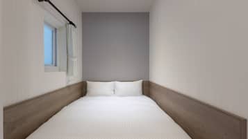 A narrow, single-bed room with a wooden headboard, a window with a curtain, and a light-colored wall.