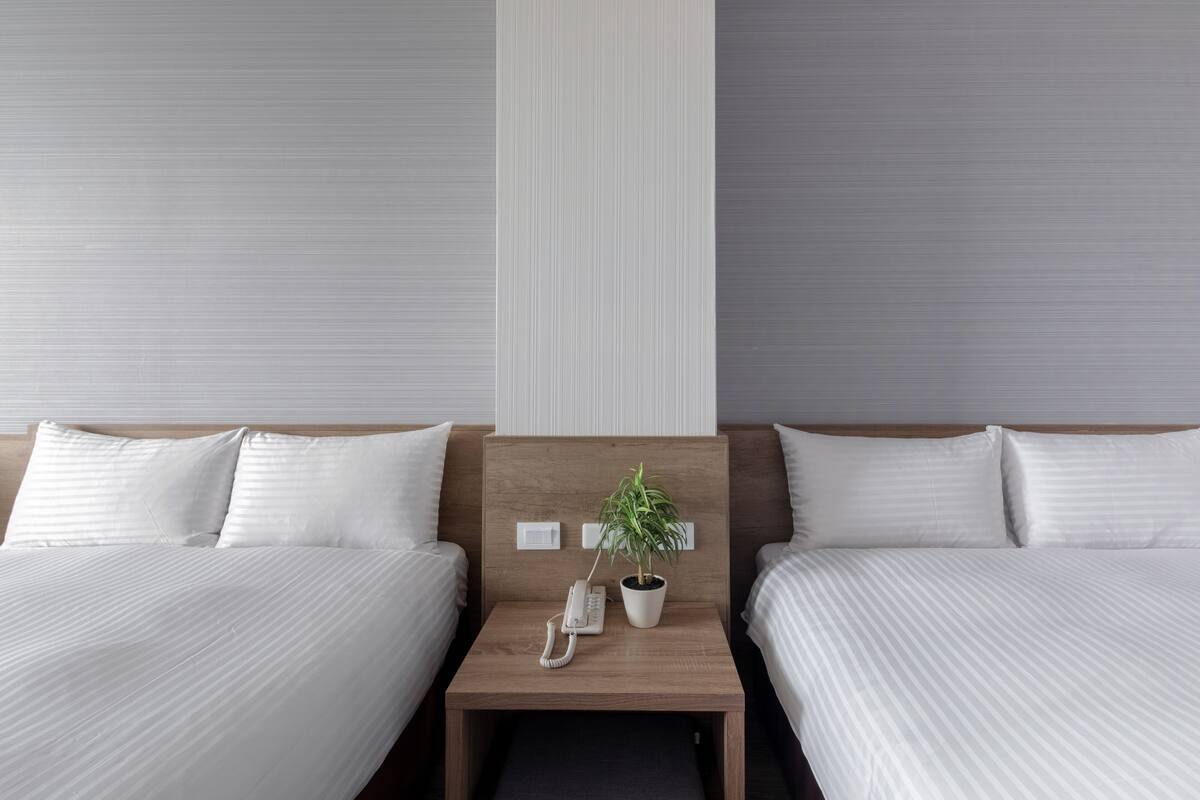 Une chambre d’hôtel avec deux lits, une table de chevet en bois sur laquelle se trouvent un téléphone et une plante, et un mur à rayures verticales.