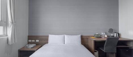 A modern hotel room with a large bed, a desk with a chair, a small cabinet, and a window with curtains.
