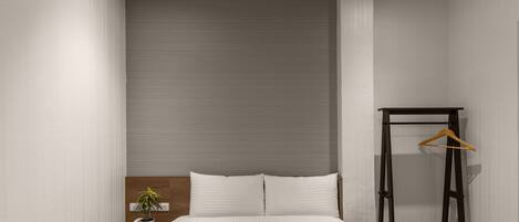 A bedroom with a bed, bedside table, and a hanging clothes rack.