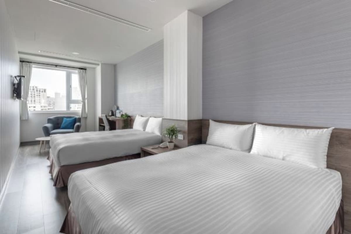 A hotel room with two beds, a desk, a chair, and a window with curtains.