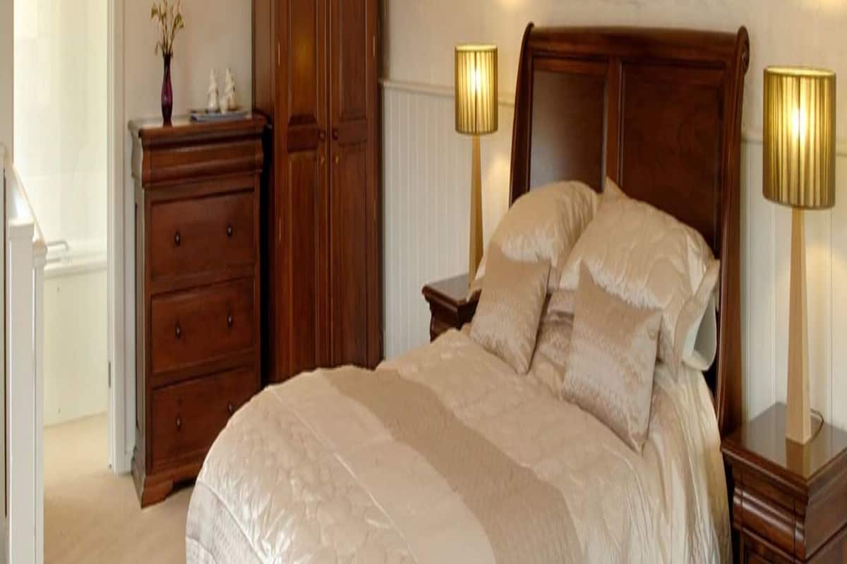 A neatly arranged bedroom with a large bed, wooden wardrobe, and bedside lamps.