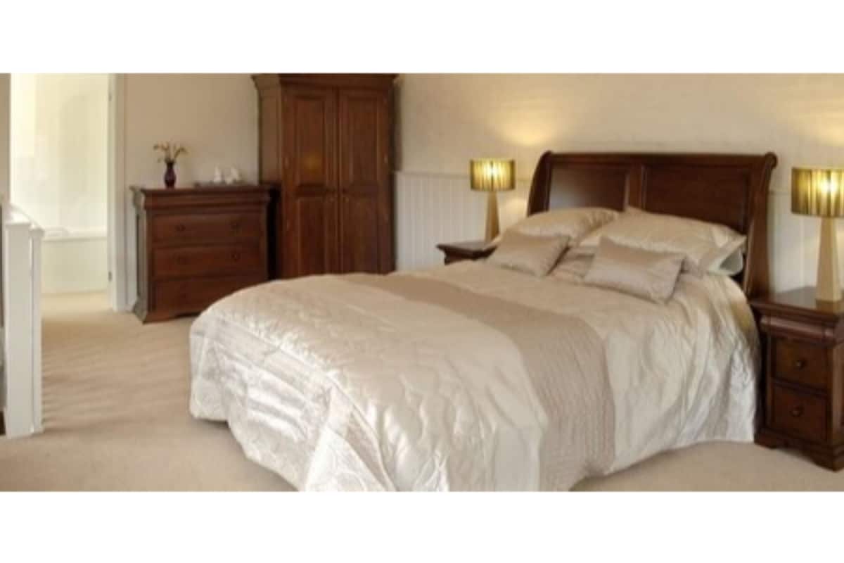 A bedroom with a large bed, wooden headboard, two bedside tables with lamps, a dresser, and a wardrobe.