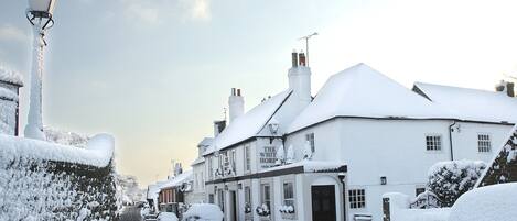Una strada innevata con un pub chiamato "The White Horse".
