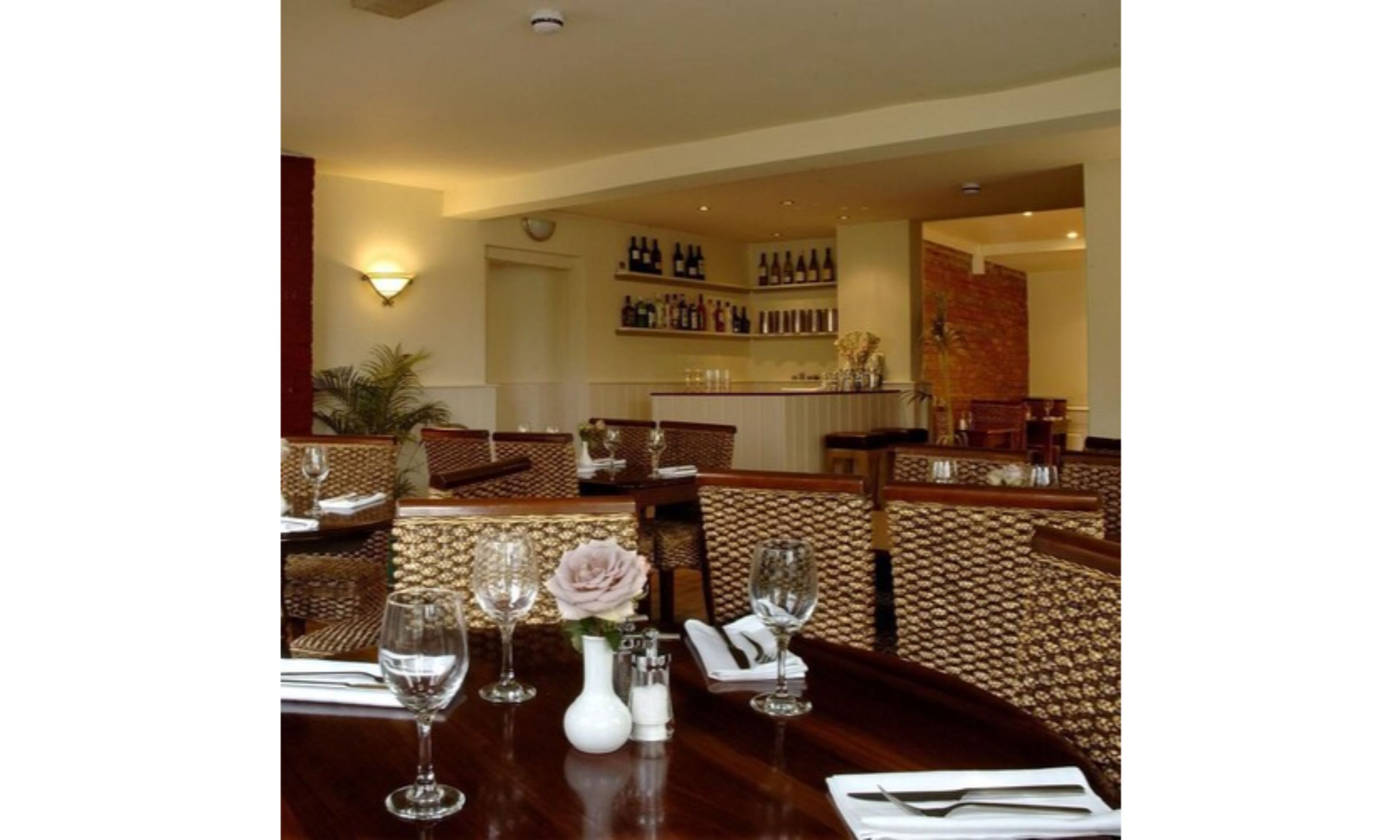 Un restaurante con sillas de respaldo alto, una mesa de madera y una copa de vino en cada lugar.