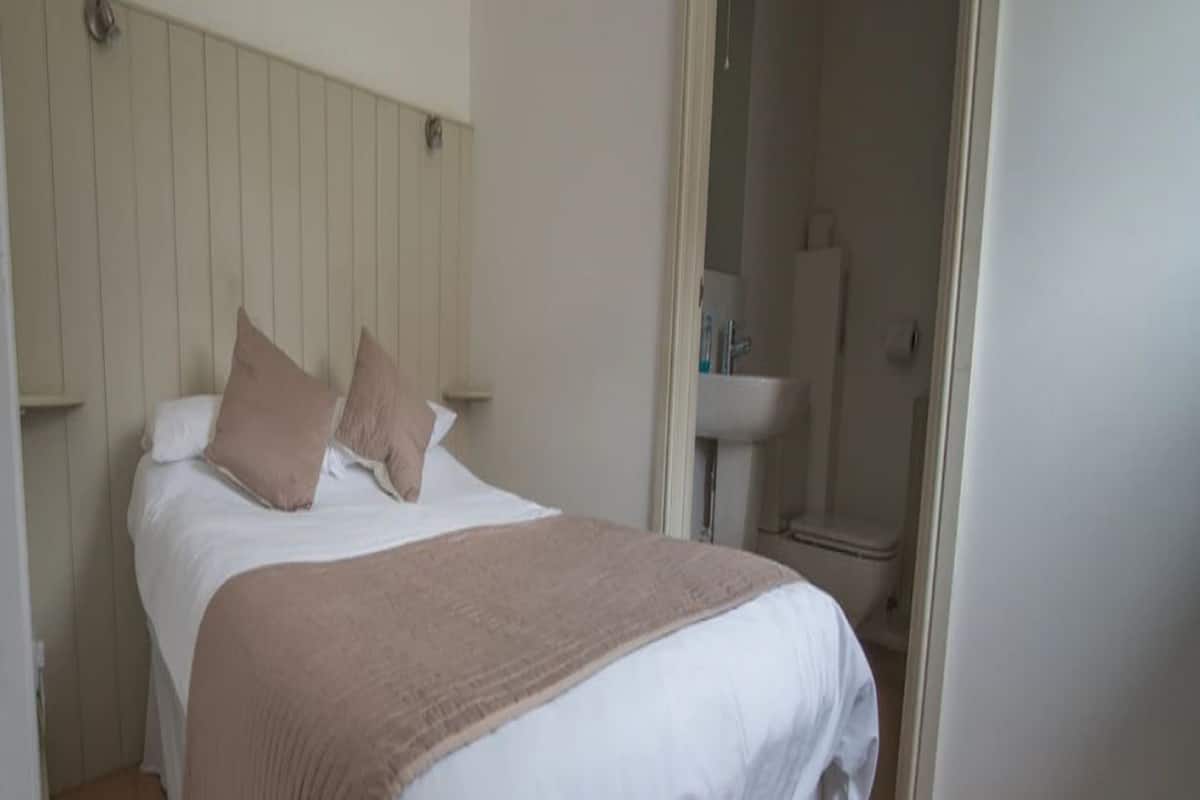 A neatly made bed with a white and beige duvet, a wooden headboard, and a beige carpet.