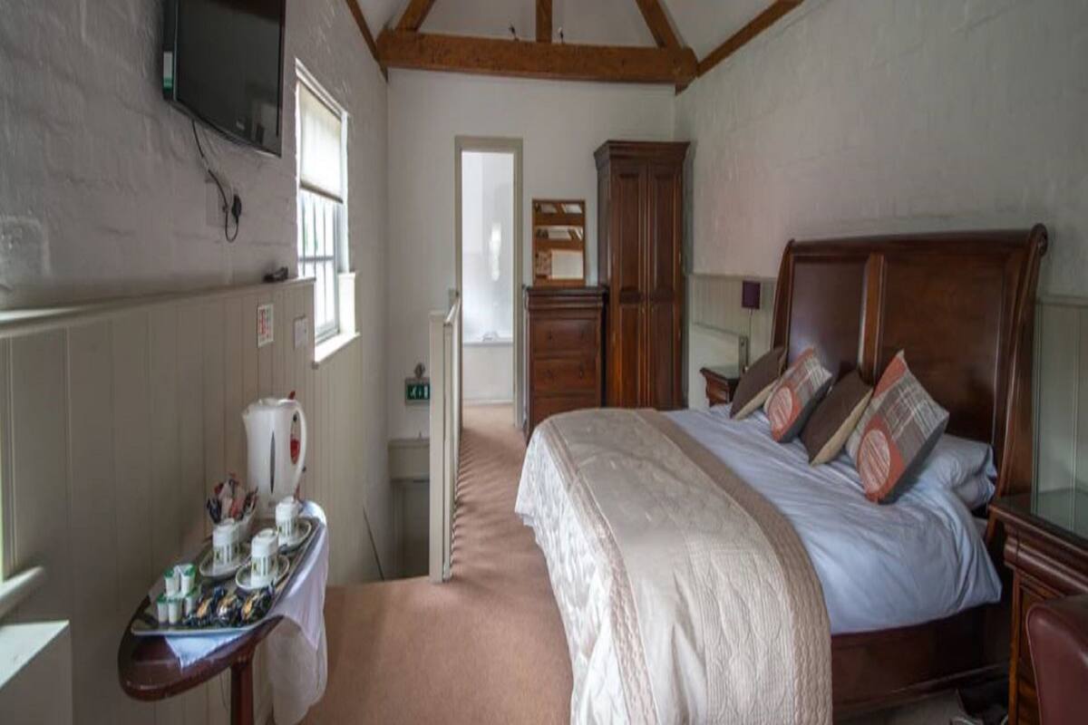 A bedroom with a wooden ceiling, a bed with a white bedspread, a wooden nightstand, a dresser, and a television mounted on the wall.