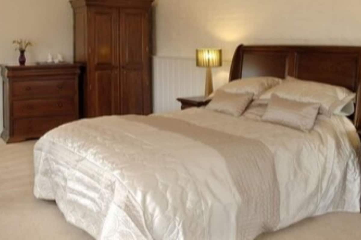 A bedroom with a large bed, wooden headboard, bedside tables with lamps, a dresser, and a wardrobe.