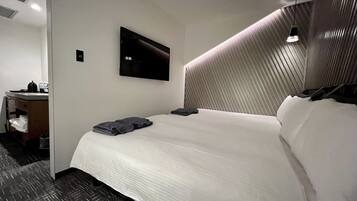 Habitación de hotel con una cama bien hecha, un televisor de pantalla plana en la pared y un escritorio con hervidor y tazas.
