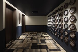 Un pasillo con alfombra estampada, una fila de ascensores y una pared con relojes enmarcados.