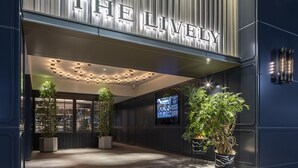 Una entrada moderna a un edificio con la señalización iluminada 'THE LIVING', plantas en macetas y una pantalla digital en la pared.