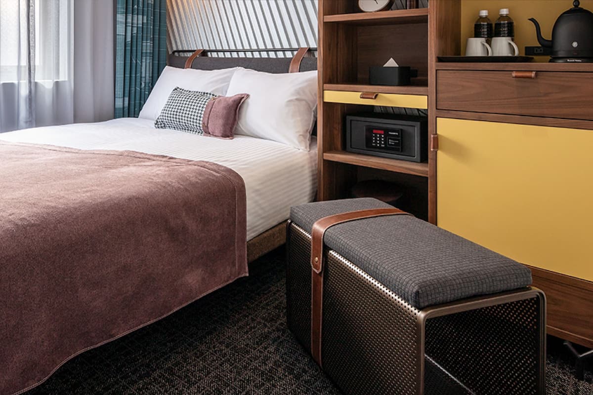 A hotel room with a bed, bedside table, and a small bench.