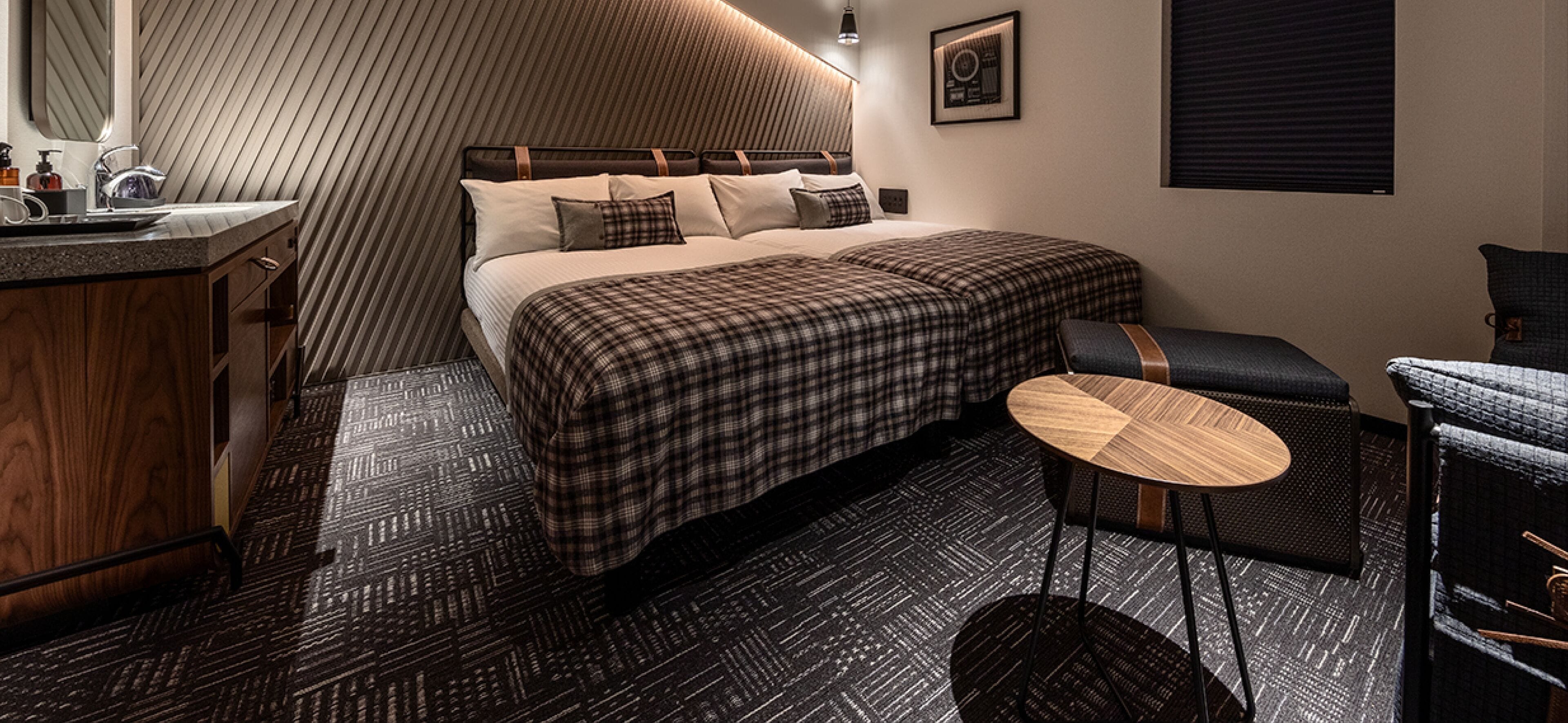 A modern hotel room with a large bed, a small round table, a wooden cabinet, and a wall-mounted picture.