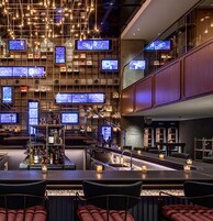 Un área de bar moderna con varias pantallas, una barra y asientos.