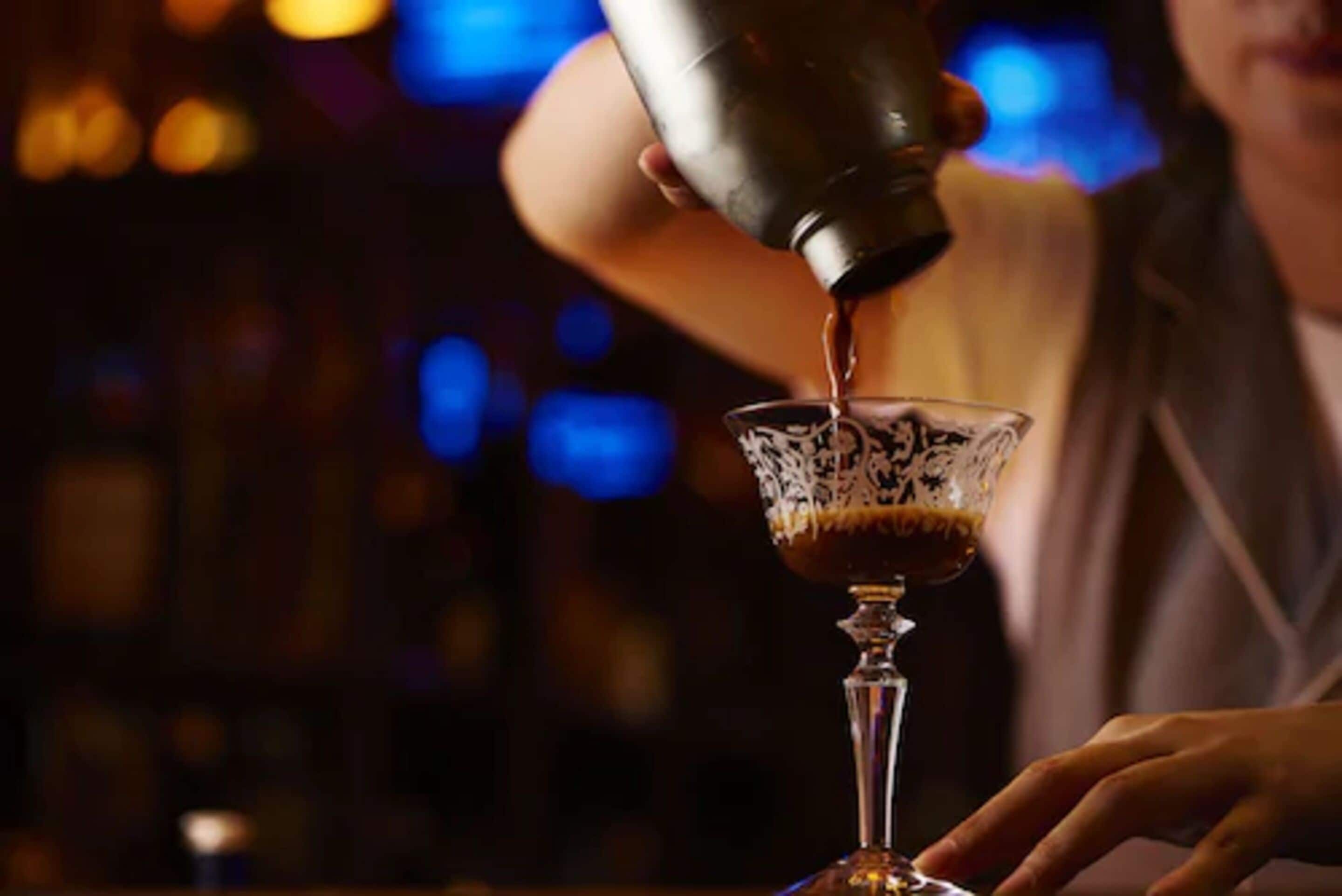 A person pouring a drink from a shaker into a glass.