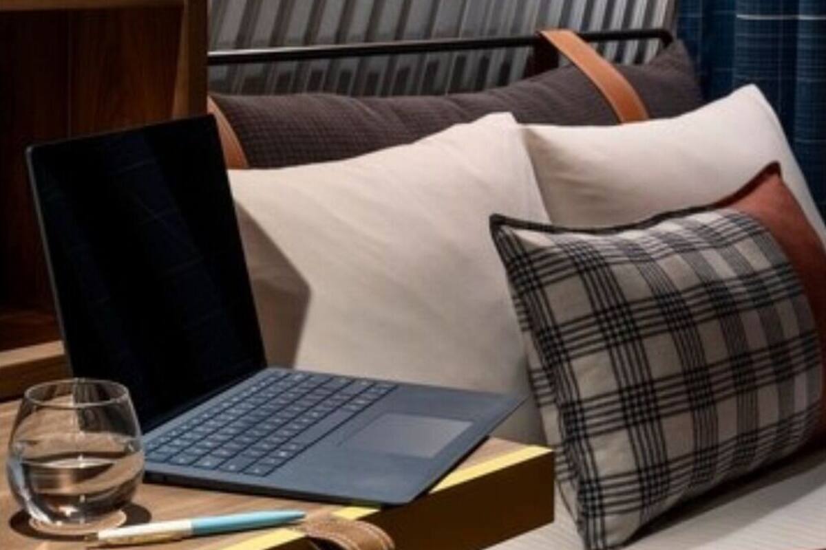 A modern bedroom with a laptop on a bedside table, a glass of water, and a pen.