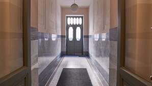 Un pasillo con paredes de mármol, una alfombra oscura y una puerta doble con diseño geométrico.