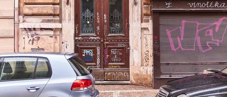 Un edificio con una entrada grande y ornamentada, un obturador cerrado con grafitis y un coche estacionado adelante.