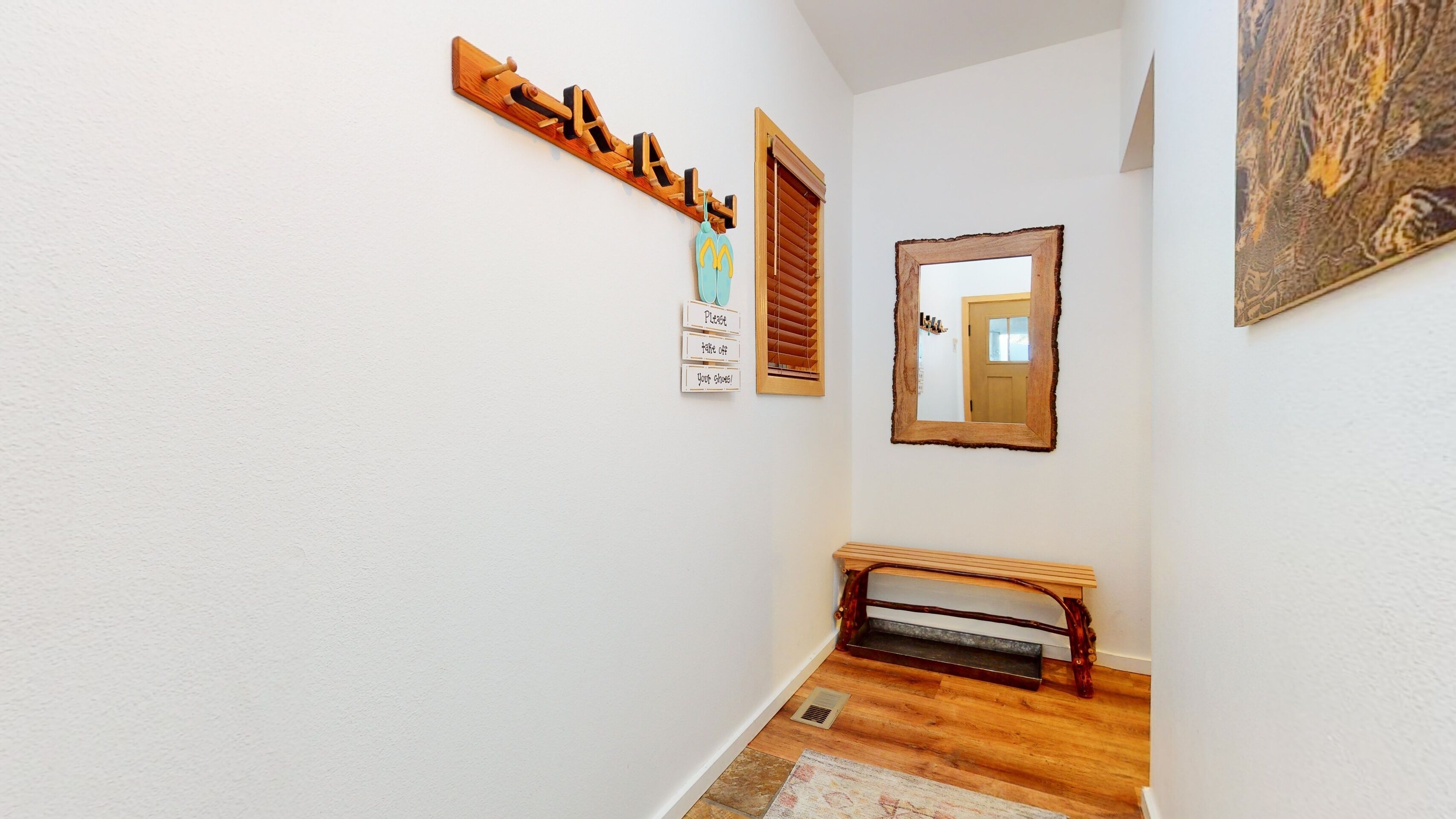 Un couloir avec un banc en bois, un miroir et une enseigne en bois portant des lettres.