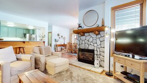 Una sala de estar con chimenea de piedra, televisor y comedor con muebles de madera.