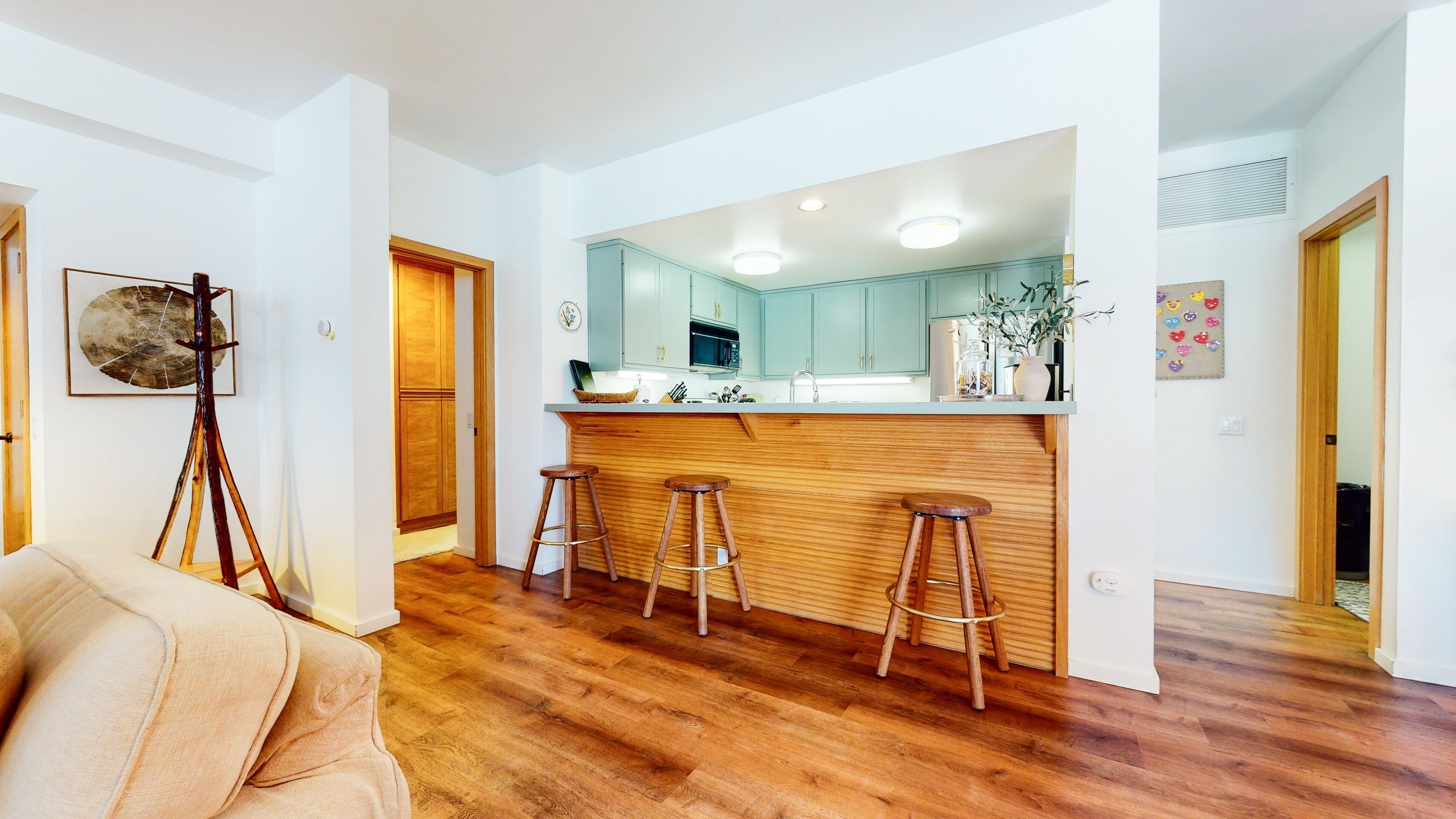 Une cuisine moderne avec des tabourets de bar en bois, un îlot central et une vue sur les pièces adjacentes.