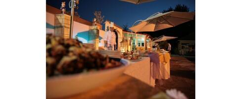 An outdoor dining area with tables and chairs, a chef, and a building in the background.