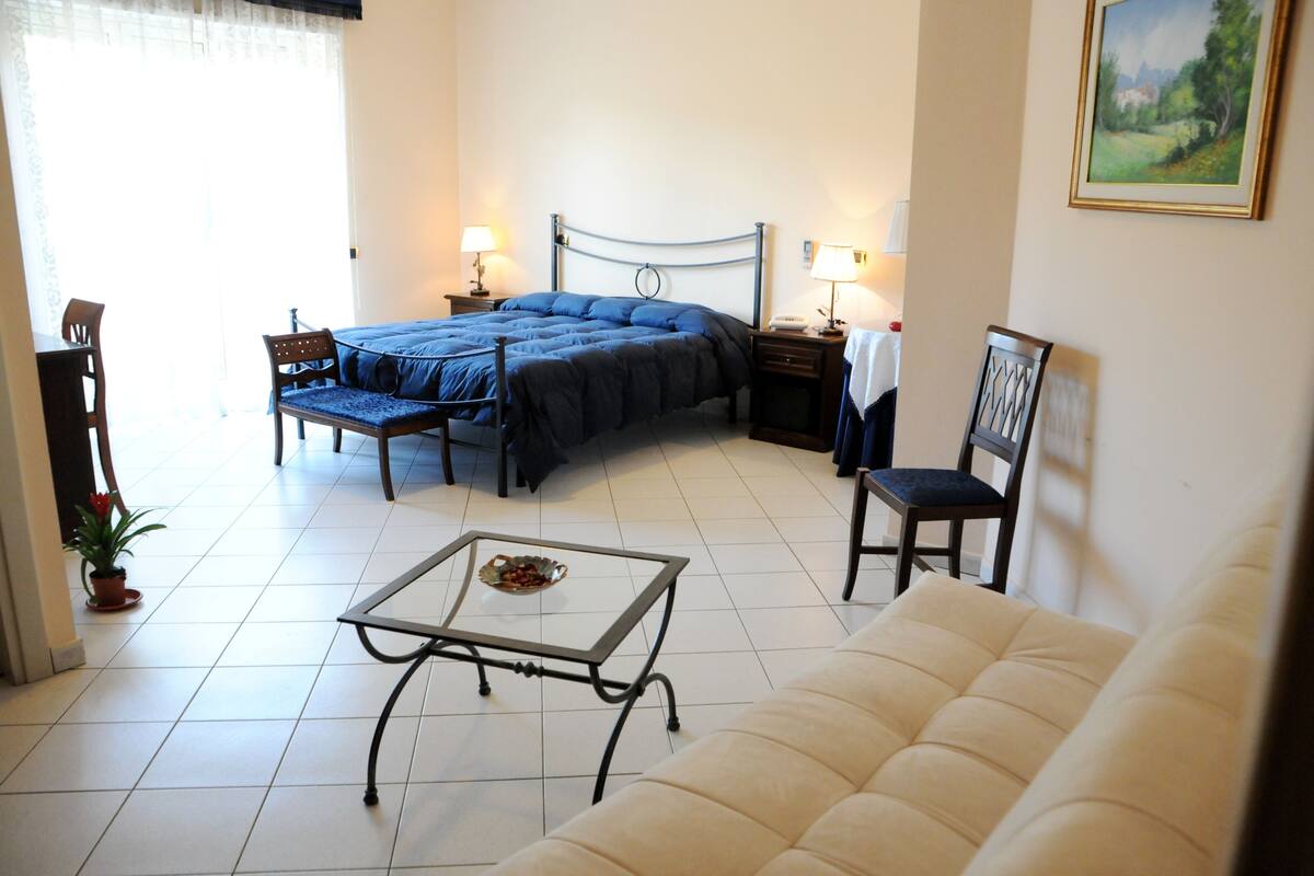 A bedroom with a bed, bedside tables, a chair, a sofa, and a small table.