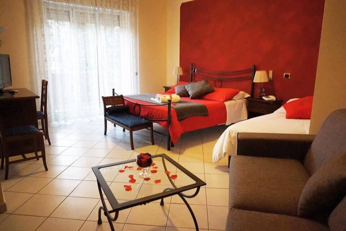 A hotel room with a bed, a desk, a chair, and a glass-top table with rose petals.