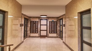 A hallway with a marble floor, a central door, and two elevator doors on either side.