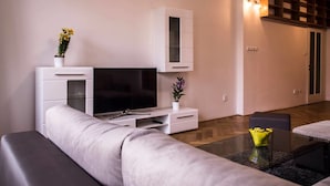 A modern living room with a flat-screen TV, white cabinetry, and a small table with a vase.
